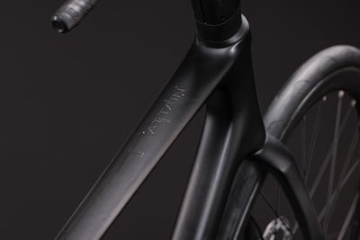 Detail eines schwarzen Rennradrahmens mit ATTAIN-Logo. Detail eines schwarzen Rennradrahmens mit ATTAIN-Logo.
