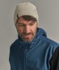 Ein Mann in einer cremefarbenen Mütze und einer blauen Kapuzenjacke mit dunklen Ärmeln.