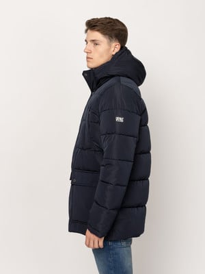 Egy férfi sötétkék kapucnis puffer dzsekiben, logóval az ujján.