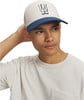 Ein Mann in einem beigen T-Shirt und einer Kappe mit einem Logo auf dem Kopf.