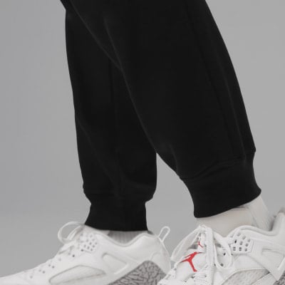 Nahaufnahme von Beinen in schwarzer Jogginghose und weißen Turnschuhen mit rotem Logo. Nahaufnahme von Beinen in schwarzer Jogginghose und weißen Turnschuhen mit rotem Logo.