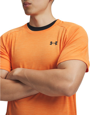 Ein Mann in einem orangefarbenen T-Shirt mit Under Armour-Logo hat verschränkte Arme. Ein Mann in einem orangefarbenen T-Shirt mit Under Armour-Logo hat verschränkte Arme.