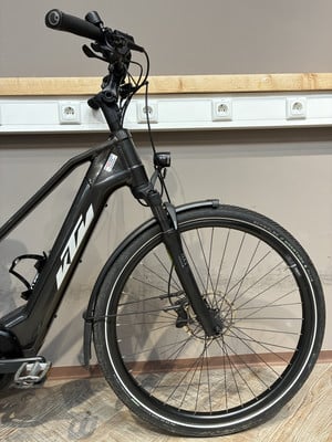 Schwarzes KTM E-Bike mit Vorderradgabel und Rad auf Holzboden. Schwarzes KTM E-Bike mit Vorderradgabel und Rad auf Holzboden.