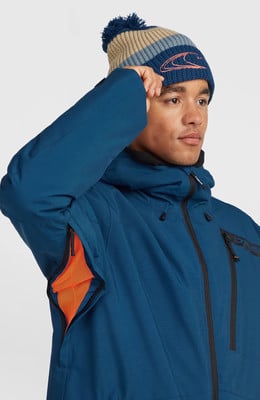 Ein Mann in einer blauen Jacke und gestreiftem Bommelhut berührt seinen Kopf.