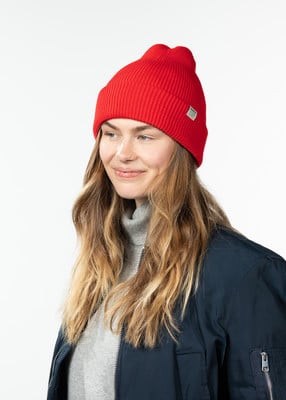 Eine Frau mit langen Haaren trägt eine rote Mütze und eine dunkle Jacke.
