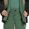 Detail einer Skijacke und Hose mit Händen in den Taschen, Grün und Schwarz.