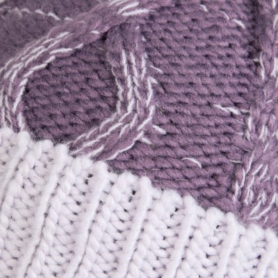 Detail eines Strickmusters mit violetten und weißen Streifen und Zöpfen.