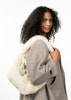 Ein Model mit lockigem Haar hält eine weiße Plüschtasche mit einem herzförmigen Anhänger.