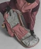 Eine Person in einer rosafarbenen Skihose öffnet einen Rucksack mit vielen Taschen.