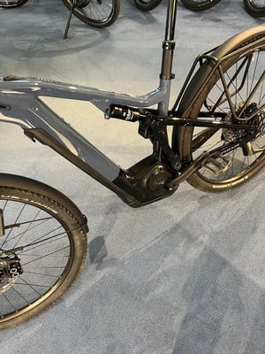 Ein graues E-Bike mit Dämpfer und Schutzblechen steht auf einem Teppich. Ein graues E-Bike mit Dämpfer und Schutzblechen steht auf einem Teppich.