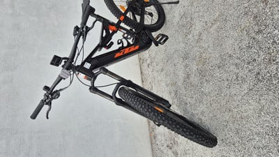 Ein schwarzes KTM Mountainbike mit orangefarbenen Akzenten steht auf grauem Untergrund. Ein schwarzes KTM Mountainbike mit orangefarbenen Akzenten steht auf grauem Untergrund.