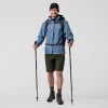 Ein Mann in blauer Jacke und Shorts hält Wanderstöcke.