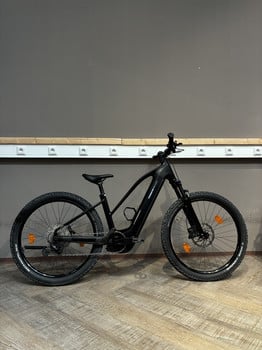 Ein schwarzes Mountainbike steht vor einer grauen Wand mit Steckdosen.
