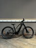 Ein schwarzes Mountainbike steht vor einer grauen Wand mit Steckdosen.