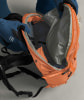 Eine Person zieht einen blauen Handschuh an und öffnet einen orangefarbenen Rucksack.