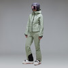 Eine Skifahrerin in grüner Kleidung und Helm mit Brille vor grauem Hintergrund.