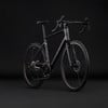 Ein schwarzes Carbon-Gravelbike mit Scheibenbremsen auf dunklem Hintergrund.