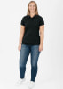 Eine Frau in einem schwarzen Poloshirt und Jeans steht vor weißem Hintergrund.