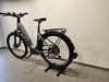 Ein graues E-Bike mit Schutzblechen und Gepäckträger steht auf dem Boden.