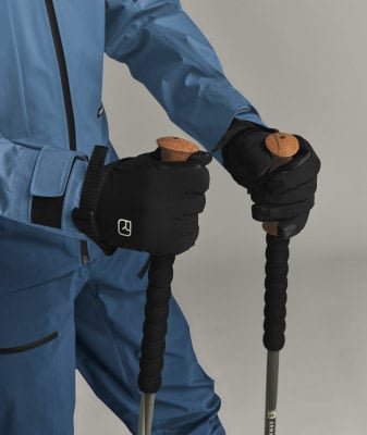 Eine Person in einer blauen Skijacke hält schwarze Handschuhe und Skistöcke. Eine Person in einer blauen Skijacke hält schwarze Handschuhe und Skistöcke.