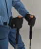 Eine Person in einer blauen Skijacke hält schwarze Handschuhe und Skistöcke.