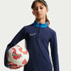 Ein Mädchen hält einen Fußball und trägt ein dunkelblaues Nike-Oberteil.