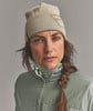 Eine Frau mit einem Zopf trägt eine beige Mütze und eine grüne Jacke.