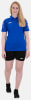 Eine Frau in einem blauen Hemd und schwarzen Shorts posiert vor weißem Hintergrund.