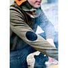Mann im grünen Pullover mit Lederflicken an den Ellbogen und buntem Schal.