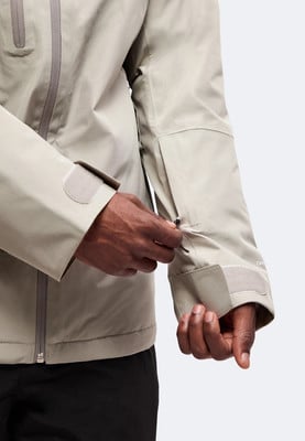 Muž si upravuje zip na rukávu světlé bundy, detailní záběr. Muž si upravuje zip na rukávu světlé bundy, detailní záběr.