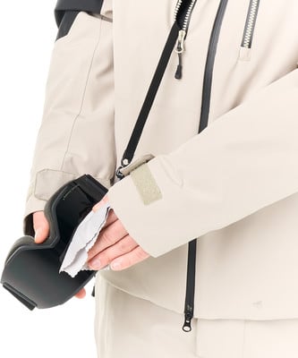 Eine Person reinigt eine Skibrille mit einem Tuch, während sie eine beige Jacke trägt.