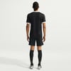 Ein Mann in schwarzem Fußballtrikot und Shorts steht mit dem Rücken.