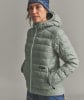 Eine Frau in einer Daunenjacke und Mütze mit ORTOVOX-Logo vor grauem Hintergrund.