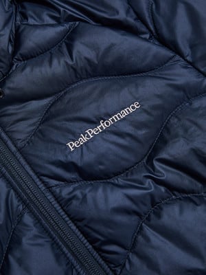 Detail einer dunkelblauen Daunenjacke mit Peak Performance Logo und Reißverschluss.