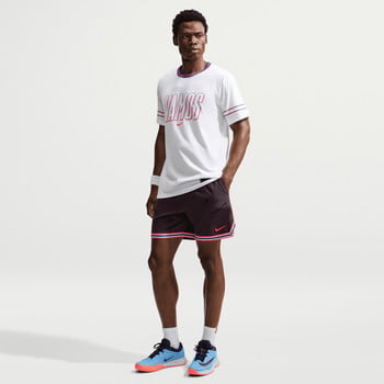 Ein Mann in einem weißen T-Shirt mit Aufdruck und schwarzen Shorts posiert.