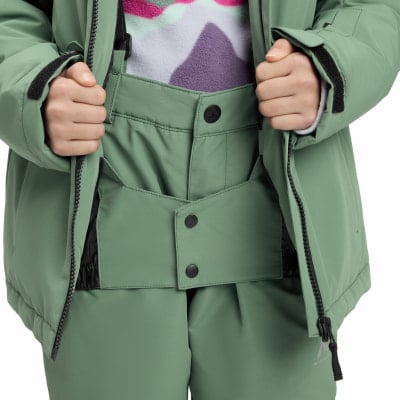 Mädchen hält eine offene Winterjacke und zeigt Latzhosen. Mädchen hält eine offene Winterjacke und zeigt Latzhosen.