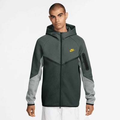 Ein Mann in einem dunkelgrünen Nike Hoodie mit gelbem Logo und grauen Ärmeln.