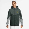 Ein Mann in einem dunkelgrünen Nike Hoodie mit gelbem Logo und grauen Ärmeln.