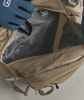 Eine Hand im blauen Handschuh legt einen schwarzen Gegenstand in eine beige Tasche.