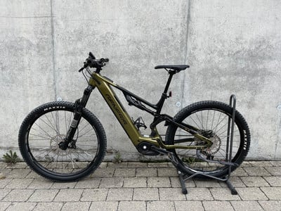 Ein grünes Genesis E-Bike steht auf einem Ständer vor einer Betonwand. Ein grünes Genesis E-Bike steht auf einem Ständer vor einer Betonwand.