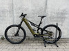 Ein grünes Genesis E-Bike steht auf einem Ständer vor einer Betonwand.