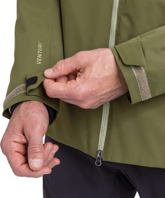 Ein Mann passt den Ärmel einer grünen Jacke mit der Aufschrift VENTURI und Klettverschluss an. Ein Mann passt den Ärmel einer grünen Jacke mit der Aufschrift VENTURI und Klettverschluss an.