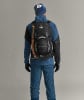 Ein Mann in blauer Jacke und Hose mit Rucksack und Eispickel.