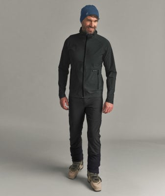Ein Mann in dunkler Jacke, Hose und blauer Mütze mit Skischuhen.
