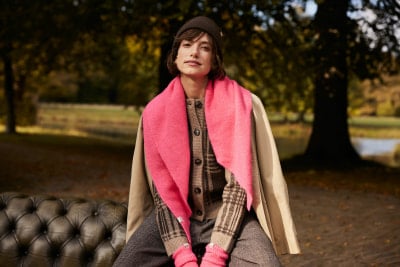 Eine Frau in einem rosa Schal und beigem Mantel sitzt auf einer Bank im Park. Eine Frau in einem rosa Schal und beigem Mantel sitzt auf einer Bank im Park.