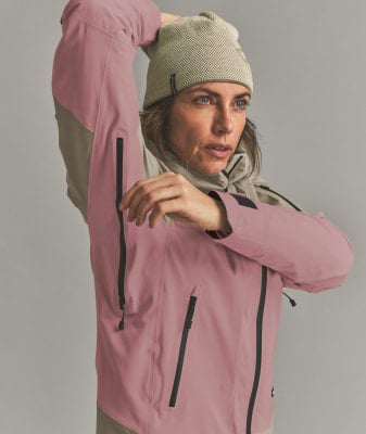 Eine Frau in einer rosafarbenen Jacke und einer beigen Mütze richtet ihre Haare. Eine Frau in einer rosafarbenen Jacke und einer beigen Mütze richtet ihre Haare.