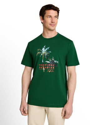 Egy férfi zöld pólóban, pálmafás mintával és „Tropical Paradise” felirattal.