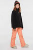 Mädchen in schwarzem Fleece-Oberteil, orangefarbener Skihose und Mütze.