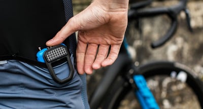 Ein Radfahrer verstaut ein blaues Gerät in der Tasche seines Radtrikots.