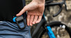 Ein Radfahrer verstaut ein blaues Gerät in der Tasche seines Radtrikots.